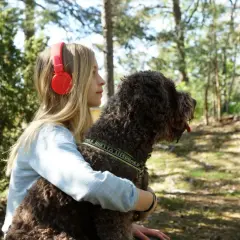 Ett barn med hörlurar kramar sin hund i skogen.