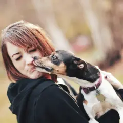En kvinna grimaserar när en hund luktar fisk och slickar henne på näsan.