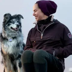 En kvinna ler mot sin border collie med blå ögon. Hunden bär ett halsband med en lysande blå enhet.