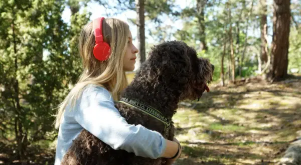 Ett barn med hörlurar kramar sin hund i skogen.