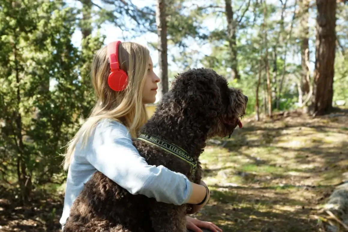 Ett barn med hörlurar kramar sin hund i skogen.