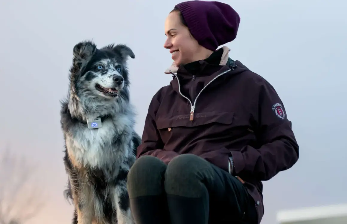 En kvinna ler mot sin border collie med blå ögon. Hunden bär ett halsband med en lysande blå enhet.