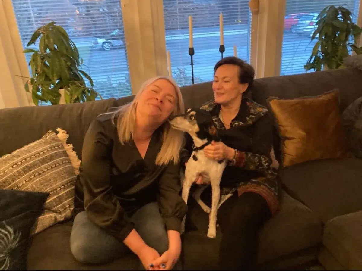 Två kvinnor och en hund sitter i soffan. En kvinna kramar hunden, som verkar trösta henne. Kanske en bild av sorg efter hund, men också kärlek.
