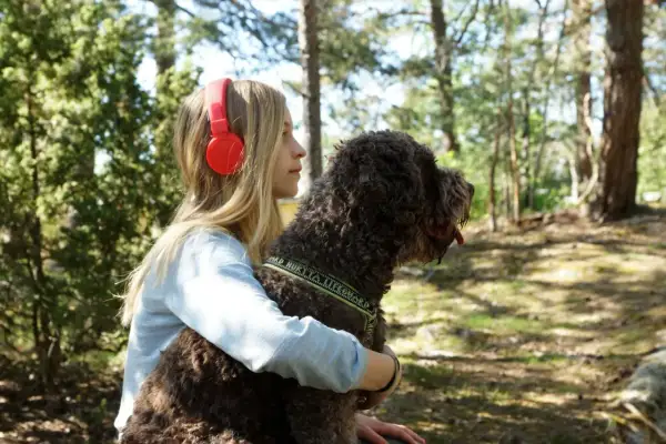 Ett barn med hörlurar kramar sin hund i skogen.