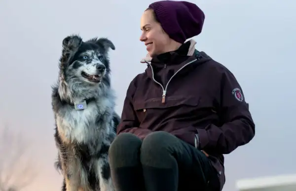 En kvinna ler mot sin border collie med blå ögon. Hunden bär ett halsband med en lysande blå enhet.